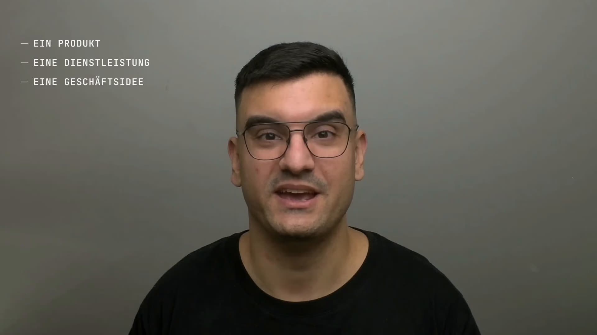 Damjan Savić spricht in die Kamera, vor einer grauen Wand